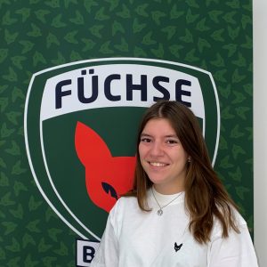 Melina Auf dem Bild sieht man Melina Haß vor dem Füchse Logo stehen. Melina absolviert ein duales Studium bei den Füchsen. Sie ist vorallem im Bereich Öffentlichkeitsarbeit zuständig.