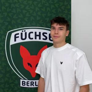 Auf dem Bild sieht man Konstantin Scholz vor dem Füchse Logo stehen. Konstantin absolviert ein duales Studium bei den Füchsen. Er ist vorallem im Bereich Fitter Fuchs zuständig.