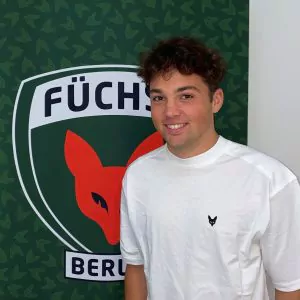 Auf dem Bild sieht man Laurin Zenger vor dem Füchse Logo stehen. Laurin absolviert ein duales Studium bei den Füchsen. Er ist vorallem im Bereich Fußball zuständig.